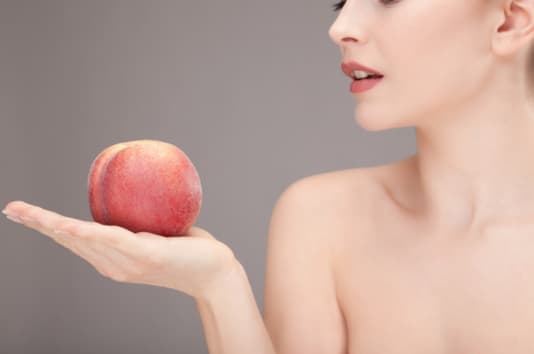 Femme nue allant croquer une pêche mûre