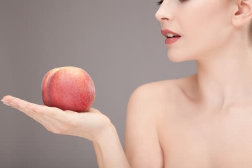 Femme nue allant croquer une pêche mûre